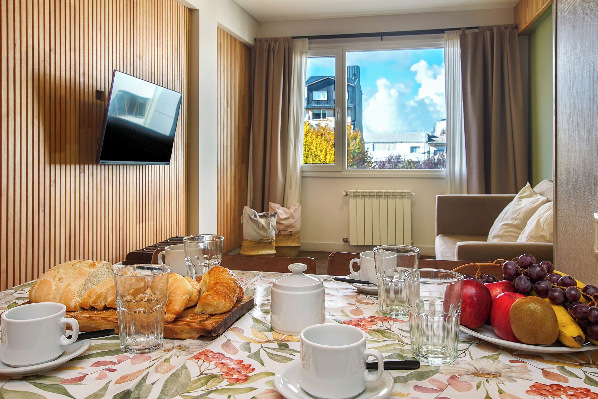 A dining area with a table set for breakfast, including croissants, fruit, and beverages.