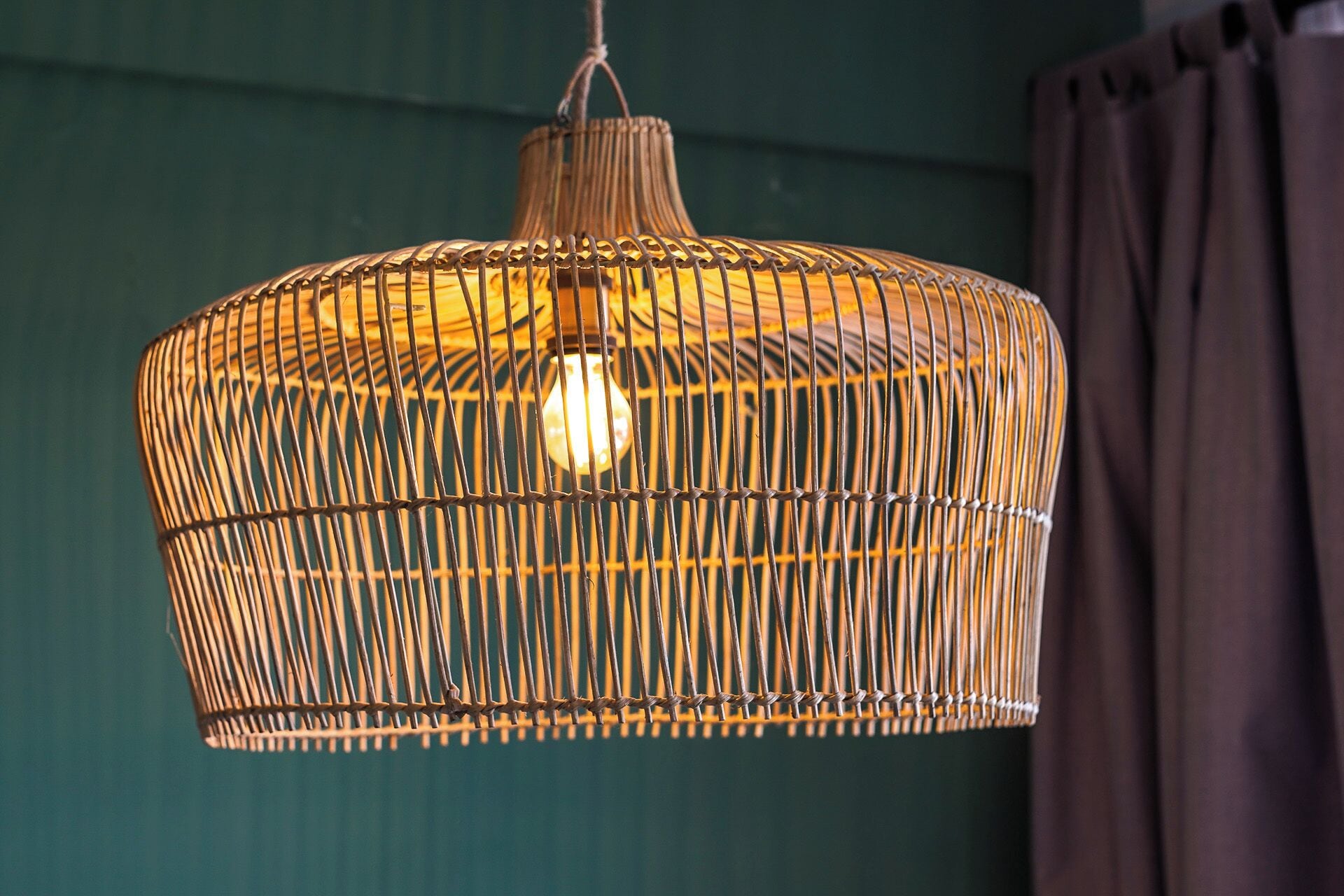 A hanging woven light fixture with a bulb inside, against a teal wall.