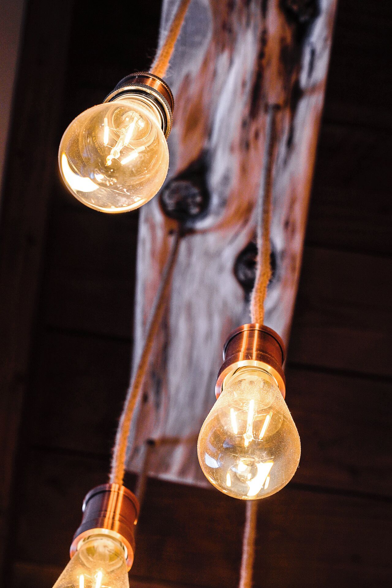 A string of vintage-style light bulbs with exposed filaments, hanging against a wooden background.