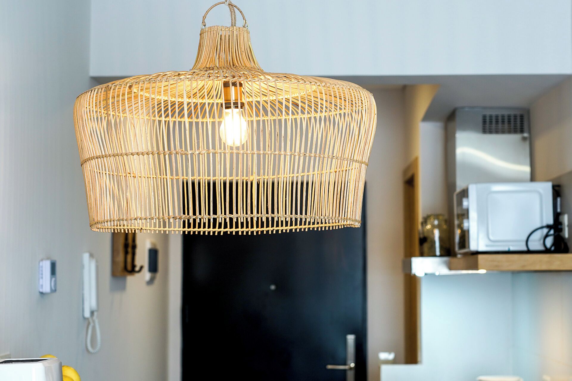 Una lámpara colgante tejida en una cocina moderna con puerta negra y electrodomésticos blancos.