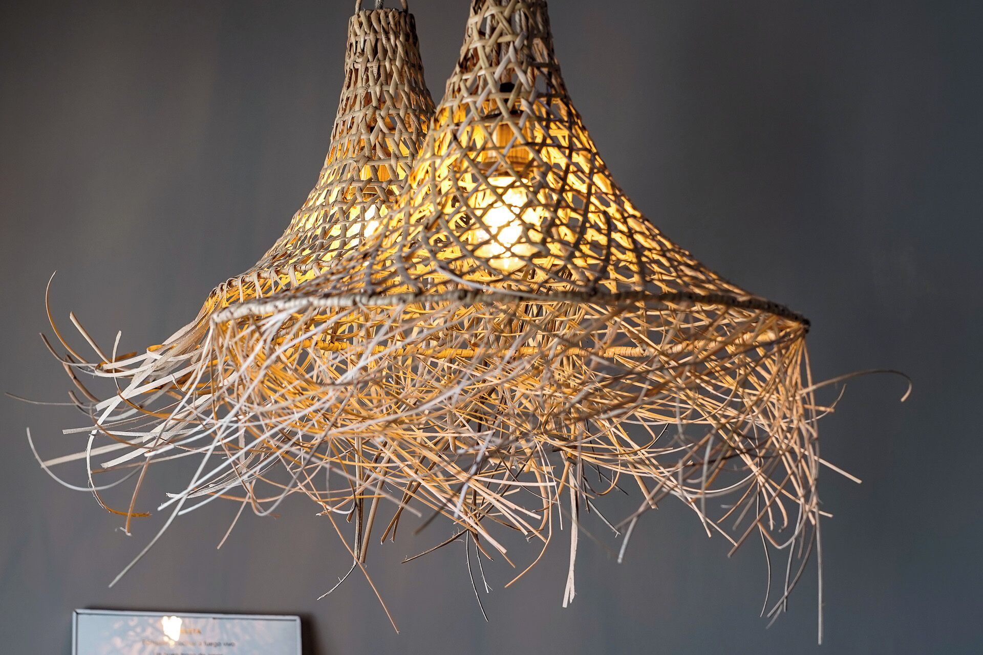 A hanging woven light fixture with a conical shape and a hanging fringe at the bottom.