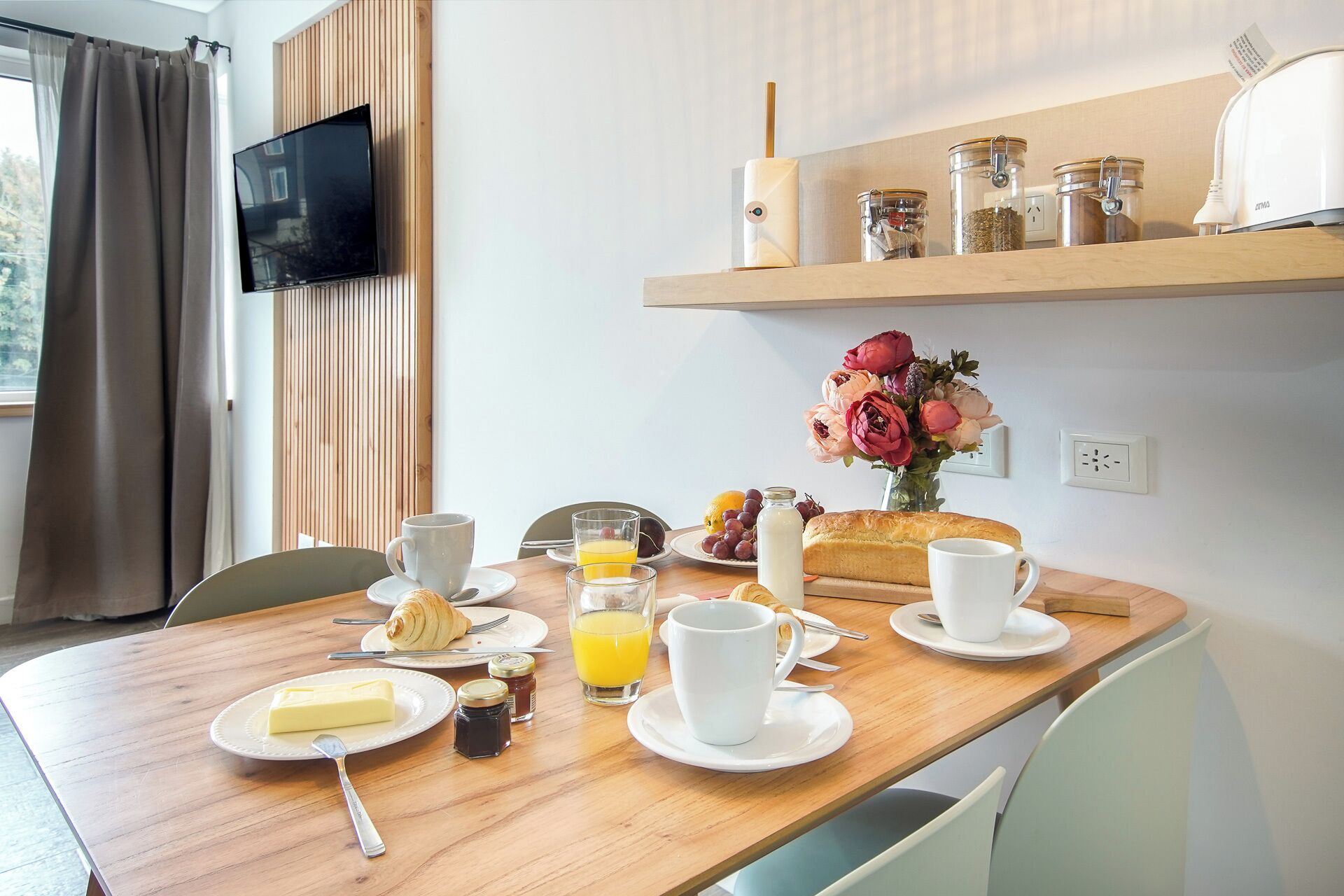 Ein Frühstücksbuffet mit Croissants, Orangensaft und einem Brotlaib auf einer Holztischplatte.