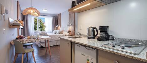 A compact kitchen with a microwave, coffee maker, and kettle. There is a dining area with a table and chairs, and a bed with a view of the outdoors.