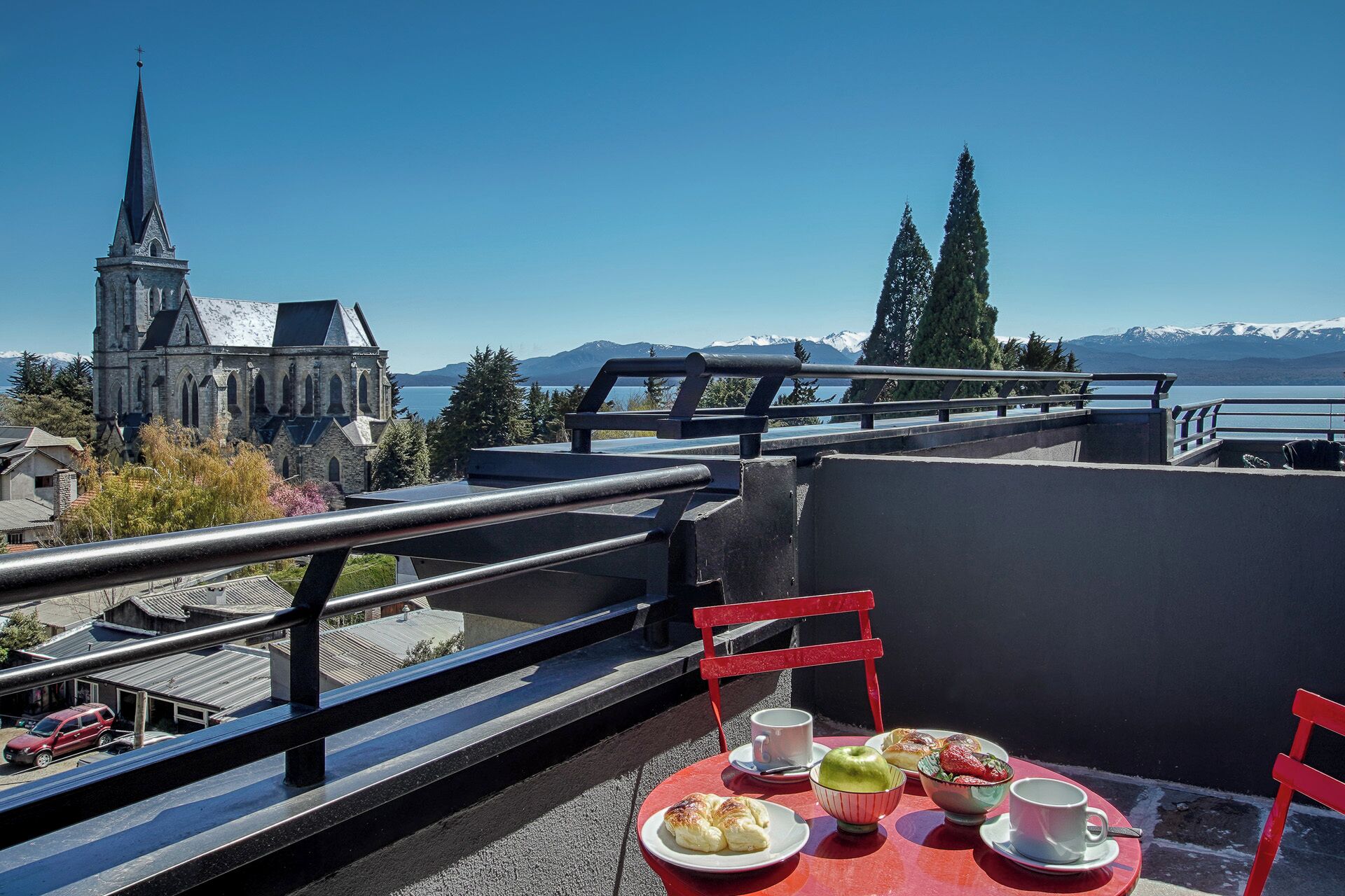 A balcony with a table set for breakfast, overlooking a church and a lake with mountains in the background.