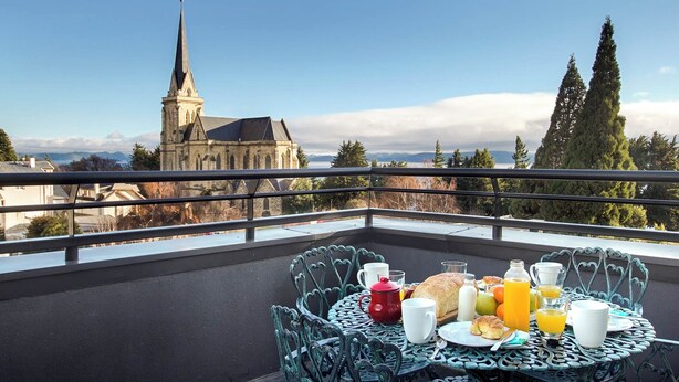 Balcón con mesa lista para el desayuno, con vista a una iglesia y montañas.