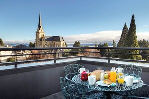 Balcón con mesa lista para el desayuno, con vista a una iglesia y montañas.