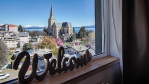 Vista de una iglesia con una aguja alta, rodeada de edificios residenciales y un lago con montañas al fondo.