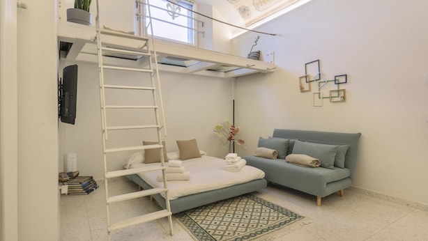 A room with a bunk bed, a sofa, a ladder, a small plant, and a decorative wall piece. - WelcHome Cellini Apartment (Firenze)