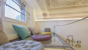 A room with a glass table, cushions, a decorative ceiling, and wall-mounted artwork. - WelcHome Cellini Apartment (Firenze)