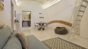 A living room with a sofa, a dining table with chairs, a bean bag, a ladder, and a decorative ceiling. - WelcHome Cellini Apartment (Firenze)