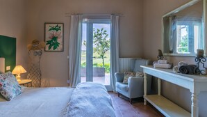 Een slaapkamer met een bed, een stoel, een nachtkastje met handdoeken, een lamp en een raam met gordijnen.