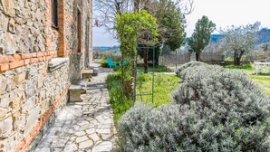 Un edificio de piedra con un estrecho sendero de piedra que conduce a un jardín con sillas verdes y una mesa.