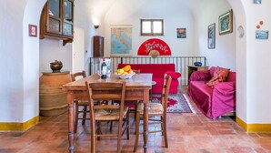 Un comedor con una mesa de madera, sillas y un sofá rojo. Hay un mapa en la pared y un ventilador.