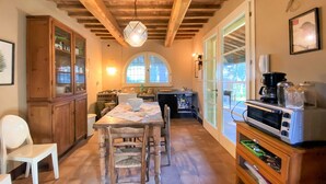 A kitchen with wooden beams, a dining table with chairs, a stove, and a coffee machine. - Vacation home Erbe by Interhome (Montescudaio)