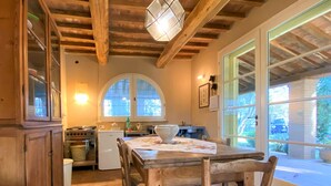 A rustic kitchen with wooden beams, a large window, and a dining table with chairs. - Vacation home Erbe by Interhome (Montescudaio)