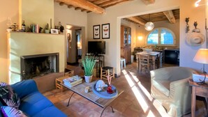 A spacious living area with a fireplace, a dining table, and a kitchen in the background. - Vacation home Erbe by Interhome (Montescudaio)
