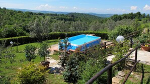 A pool with a blue and white exterior, surrounded by a lush garden and a scenic view of rolling hills.