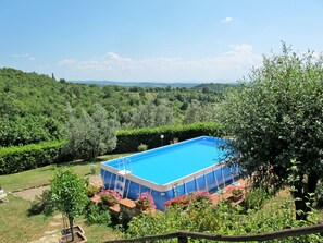 Una piscina rectangular con revestimiento azul, rodeada de abundante vegetación y un paisaje montañoso al fondo.