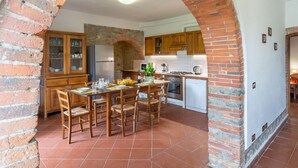 A kitchen with a brick archway, wooden cabinets, a dining table set for six, and a tiled floor. - Podere Ritali by Interhome (Civitella in val di Chiana)