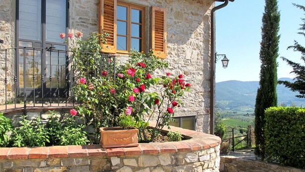 A stone building with wooden shutters, a potted plant with red flowers, and a view of the countryside. - San Rocco by Interhome (Greve in Chianti)