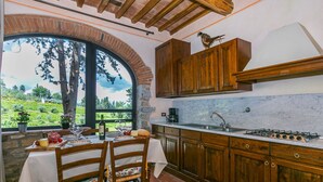 A rustic kitchen with wooden cabinets, a marble countertop, and a large window overlooking a garden. - San Rocco by Interhome (Greve in Chianti)