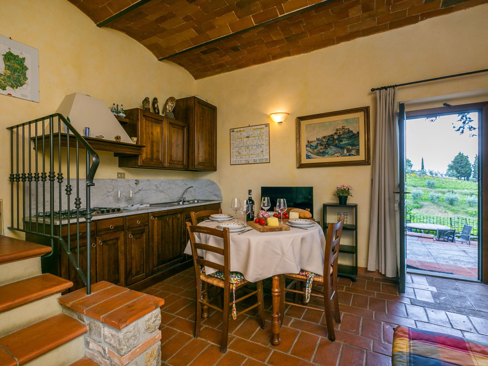Une cuisine chaleureuse, avec des meubles en bois, un plan de travail en marbre et un coin repas où une table est dressée pour deux personnes.