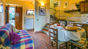 A cozy living room with a plaid sofa, a dining table set with wine glasses and plates, and a staircase leading to a kitchen area with a wooden railing. - San Rocco by Interhome (Greve in Chianti)