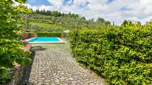 A pool area with a stone pathway leading to a rectangular pool, surrounded by lush greenery and a stone wall. - San Rocco by Interhome (Greve in Chianti)
