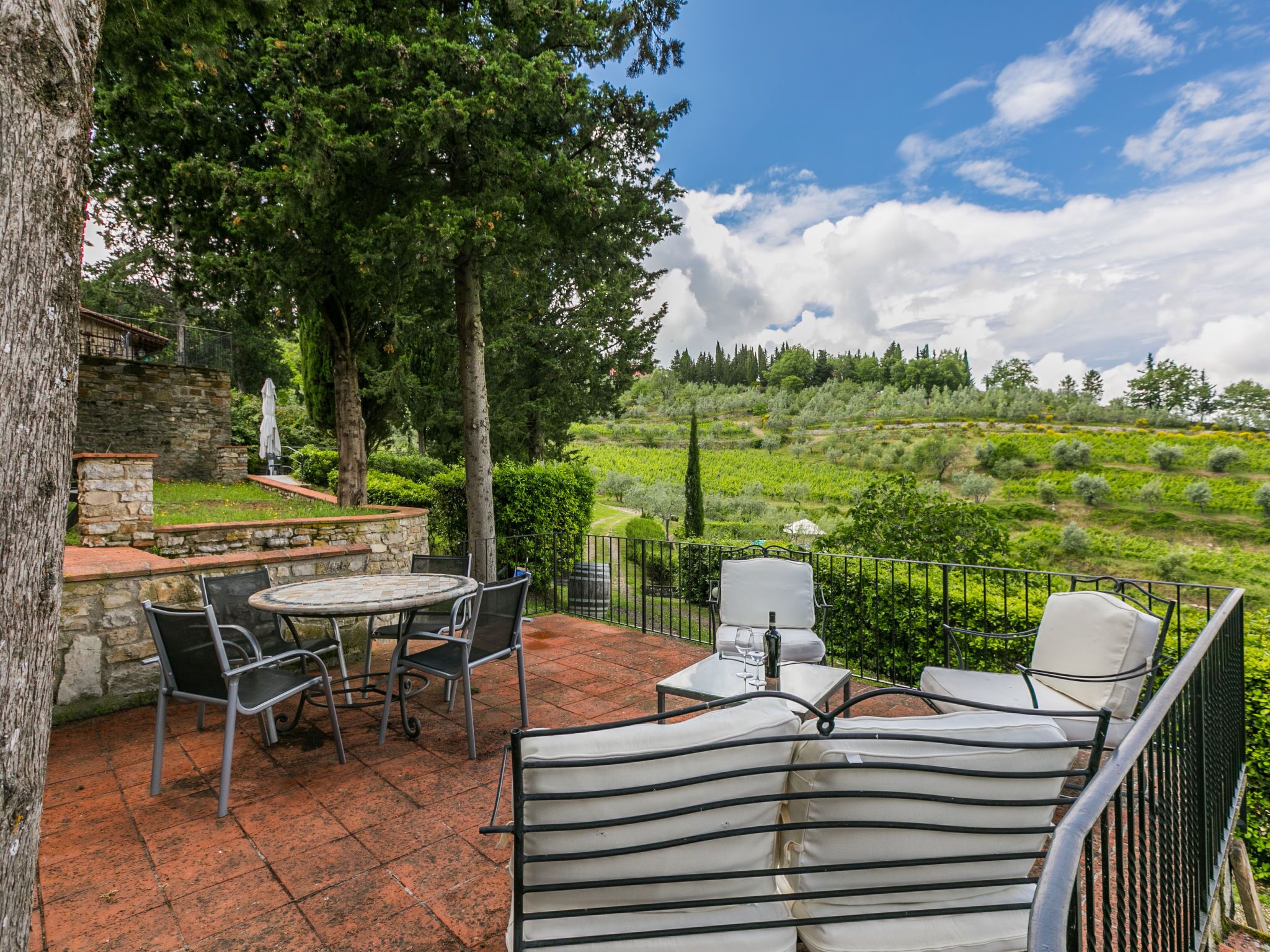 An outdoor patio with a stone wall, a round table, and chairs.