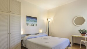 Ein Schlafzimmer mit Bett, Nachttisch, Stuhl und Schreibtisch mit Pflanze.