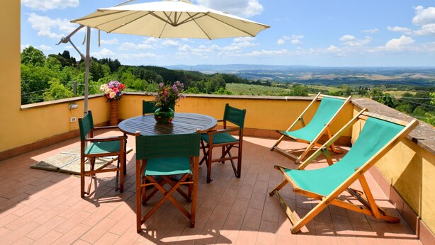 Eine Terrasse mit Tisch und Stühlen, einem großen Sonnenschirm und Blick auf die Landschaft.
