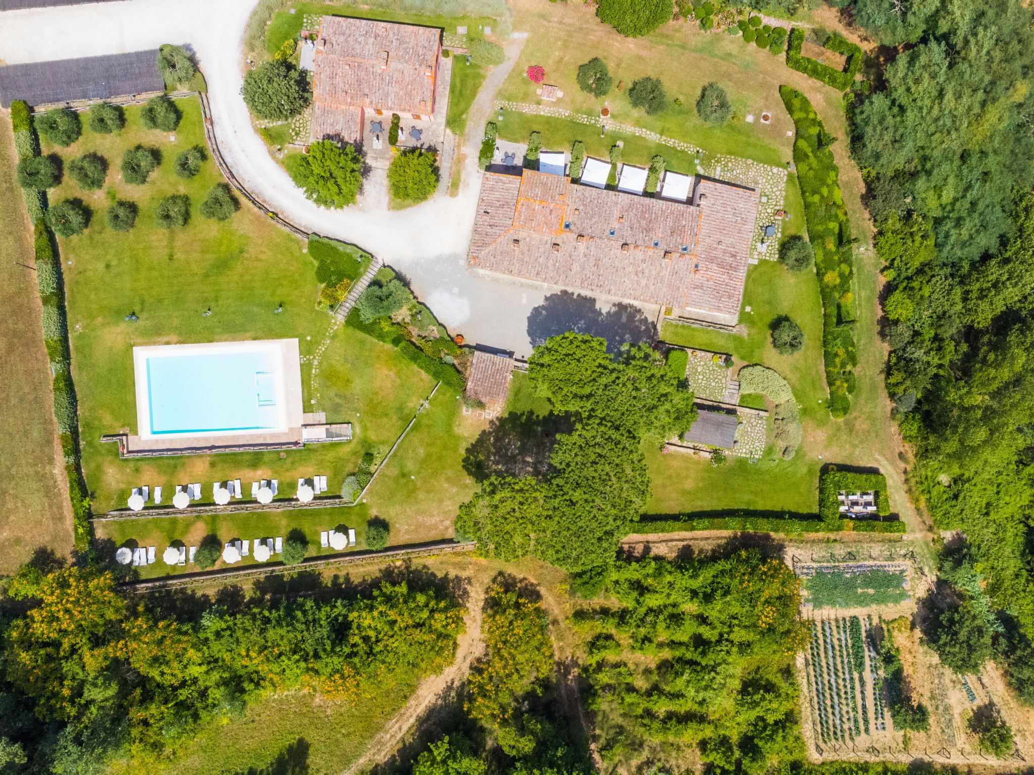 An aerial view of a property with a swimming pool, tennis courts, and a large building with a tiled roof.