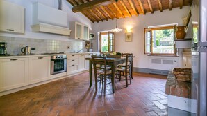 A kitchen with white cabinets, a herringbone-patterned floor, a wooden ceiling, and a dining area with a table and chairs. - Francigena by Interhome (Castelfiorentino)