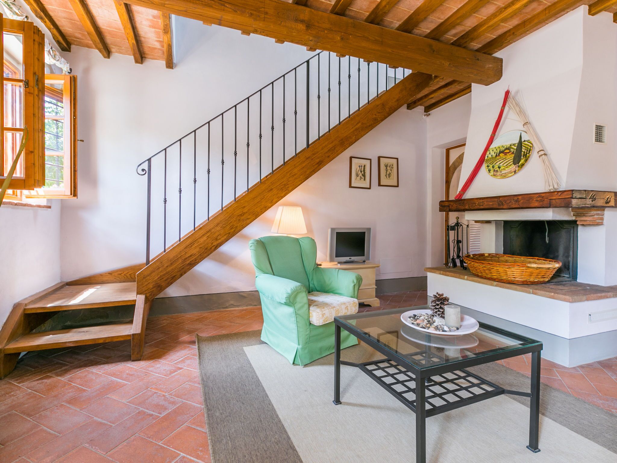 A cozy living room with a wooden staircase, a green armchair, a glass coffee table, and a fireplace.