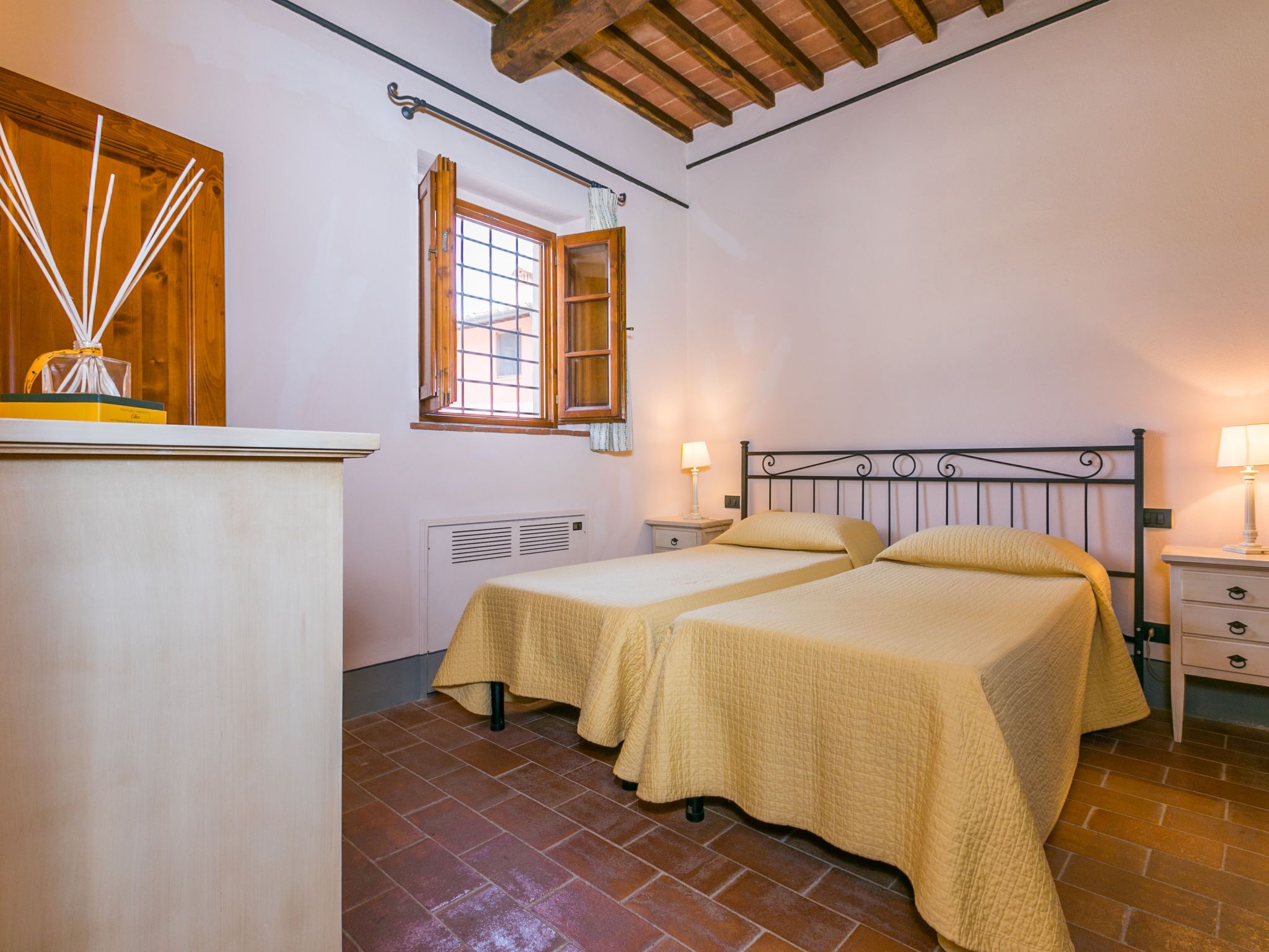 Un dormitorio con dos camas, cabecero de madera, una ventana, un radiador y una mesita de noche con lámpara.