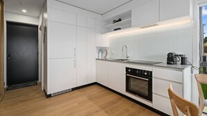 Una cocina moderna con armarios blancos, horno empotrado y cafetera.