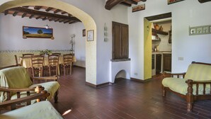 Un coin repas avec des chaises en bois et une table, une cuisine aux carreaux décoratifs et un plafond rustique avec des poutres apparentes.