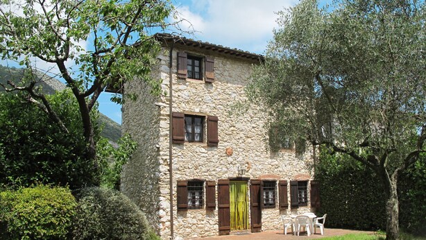Un bâtiment en pierre avec un toit en tuiles, des volets en bois et un petit patio aménagé avec du mobilier d’extérieur.