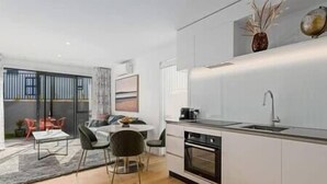 A modern kitchen with a built-in oven and a sink. There is a dining area with a table and chairs. - Explore Wanaka - Mountain Views, Riverside Locale (Albert Town)