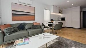 A modern living room with a grey sofa, a coffee table, and a dining area with a small table and chairs. - Explore Wanaka - Mountain Views, Riverside Locale (Albert Town)
