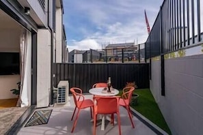 A patio with a round table and four chairs, a small heater, and a green lawn area.