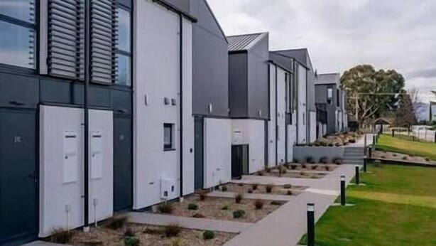 A modern building with a series of white and grey structures, likely residential units, with a flat roof and a small garden area in front. - Explore Wanaka - Mountain Views, Riverside Locale (Albert Town)