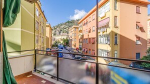 Un balcone con vista su una stretta via fiancheggiata da edifici colorati, un cielo sereno e auto parcheggiate.