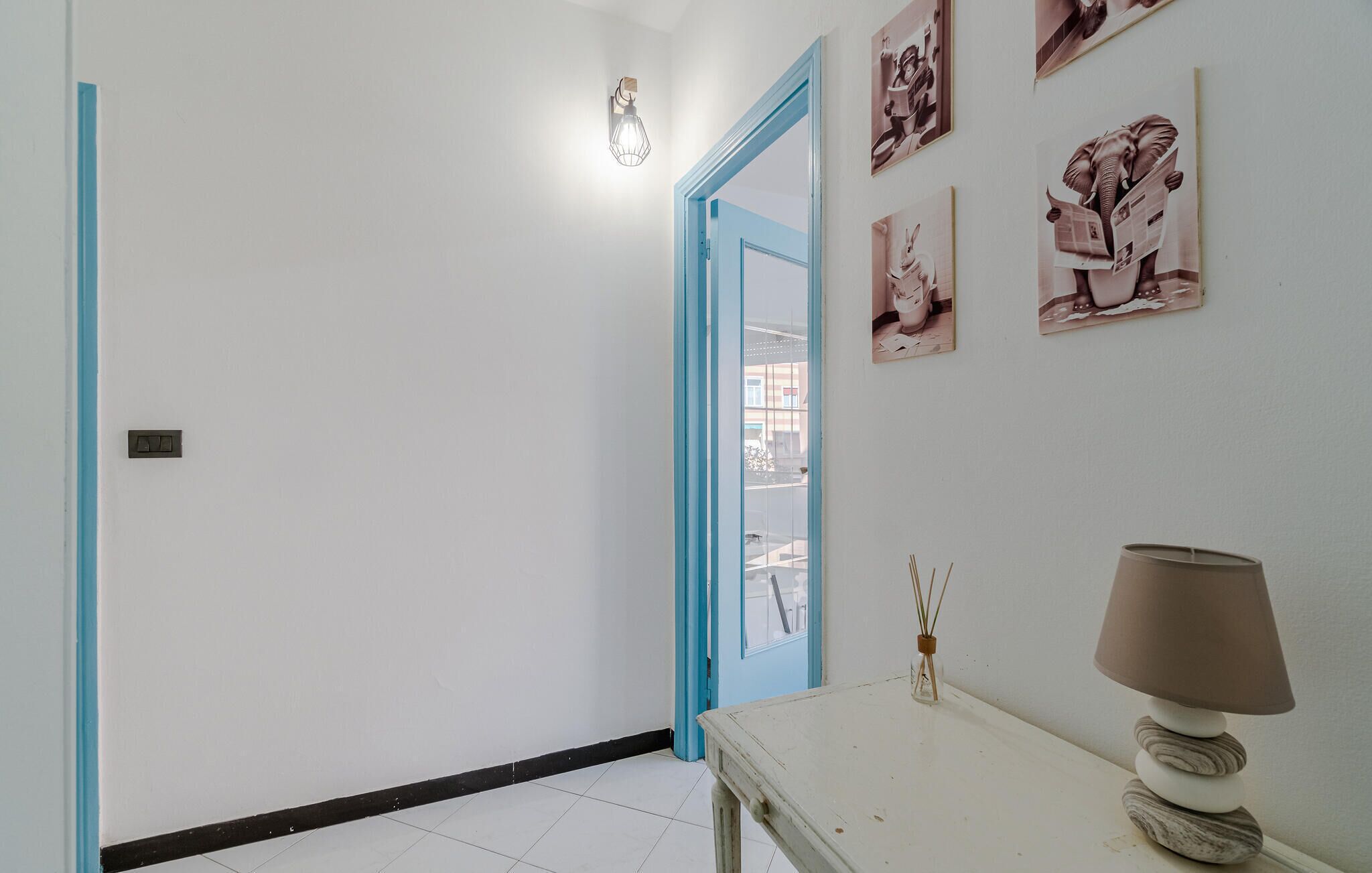 A hallway with a blue door, a table with a lamp, and wall art.