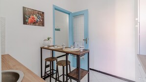 Una piccola sala da pranzo con un tavolo apparecchiato per due, una porta blu e un cartello al muro con la scritta 'Farm Fresh Locally Grown'.