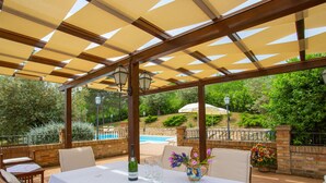 An outdoor patio with a table set for dining, surrounded by chairs, and a pergola overhead.