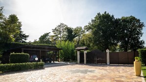 A paved driveway leading to a gated entrance with a covered carport and a potted plant.