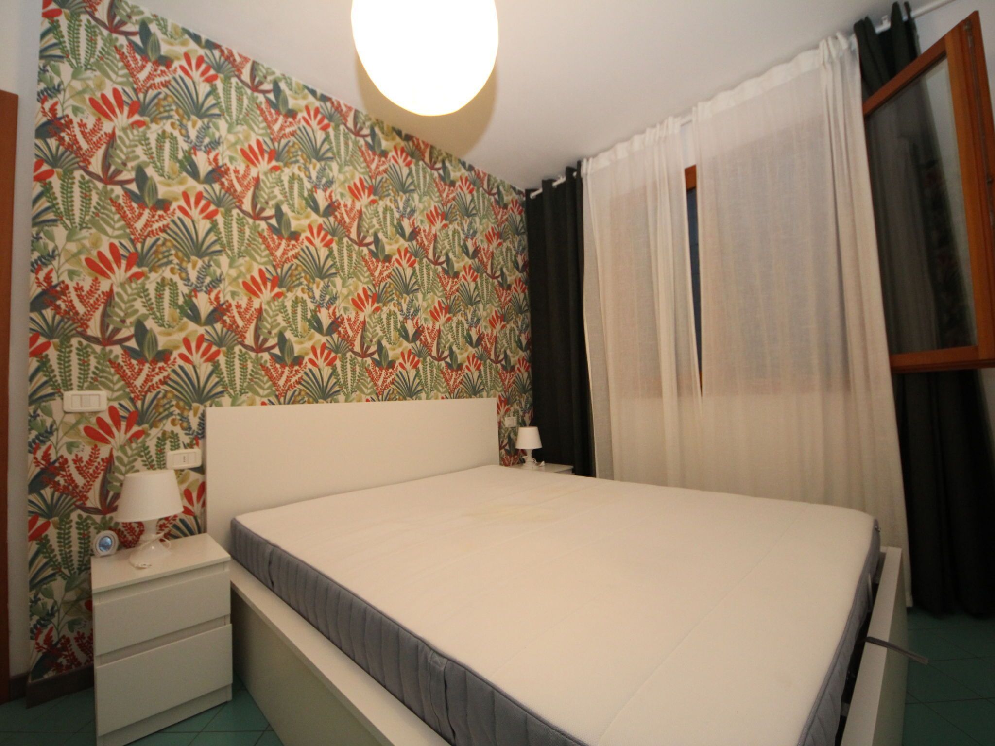 A bedroom with a bed, a nightstand, a lamp, and a wall with a floral pattern.