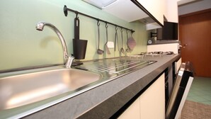 A kitchen with a stainless steel sink, a gas stove, and hanging utensils. - Solmare by Interhome (Rosolina Mare)