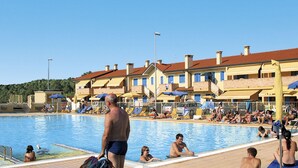 A swimming pool area with people sunbathing and swimming, surrounded by multi-story buildings with balconies. - Solmare by Interhome (Rosolina Mare)